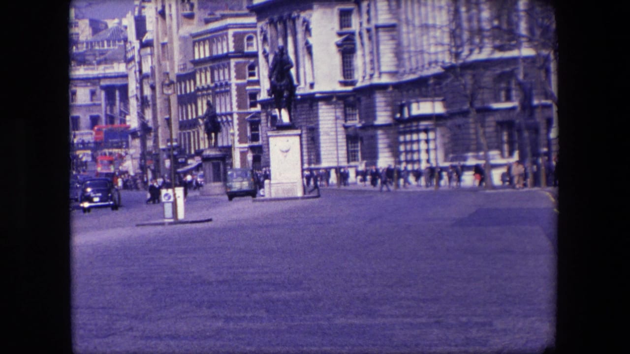 Wide city roadway with cars, pedestrians, a statue, and stone buildings.