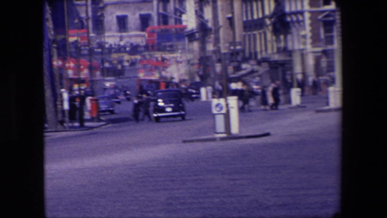 London street with cars, pedestrians, red buses, and older buildings in soft 8mm focus.