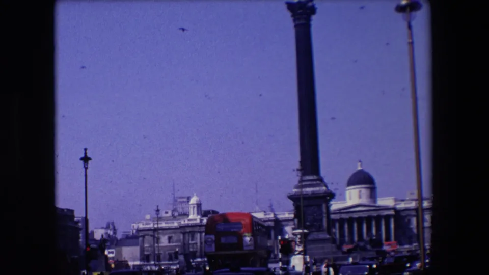1967 London view across an open urban space with a tall column-like monument, red bus, cars, street lamps, and a domed building visible beyond the roadway.