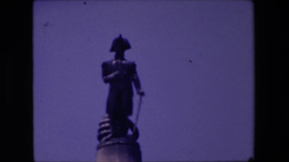 Low-angle 1967 London travel frame showing a standing public statue above a pedestal, filmed in soft focus on 8mm stock.
