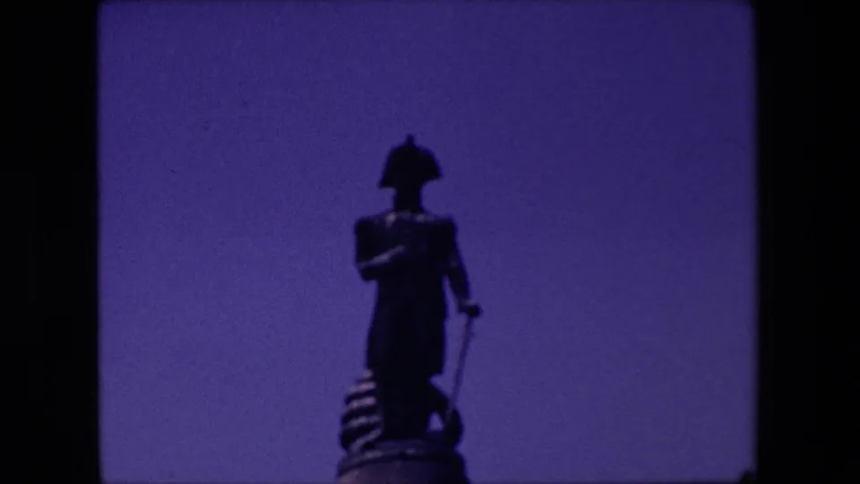 Final frame of the short 8mm clip showing the statue figure and pedestal against a blue-purple sky with slight blur and grain.