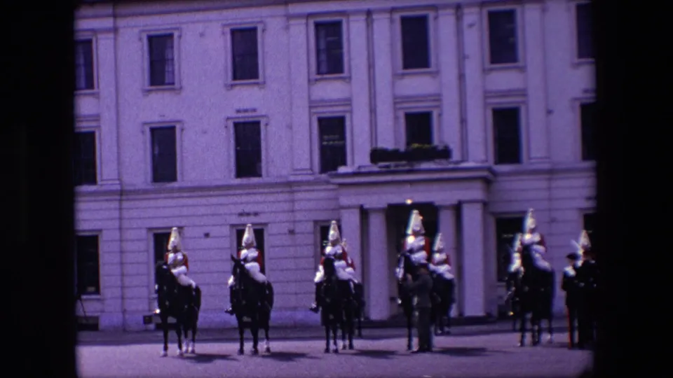 In supplied 1967 London footage, mounted cavalrymen in red and metal full-dress uniforms line up before a pale building facade.