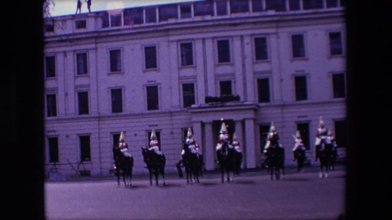Mounted soldiers in dress uniform stand in formation before a pale stone building.