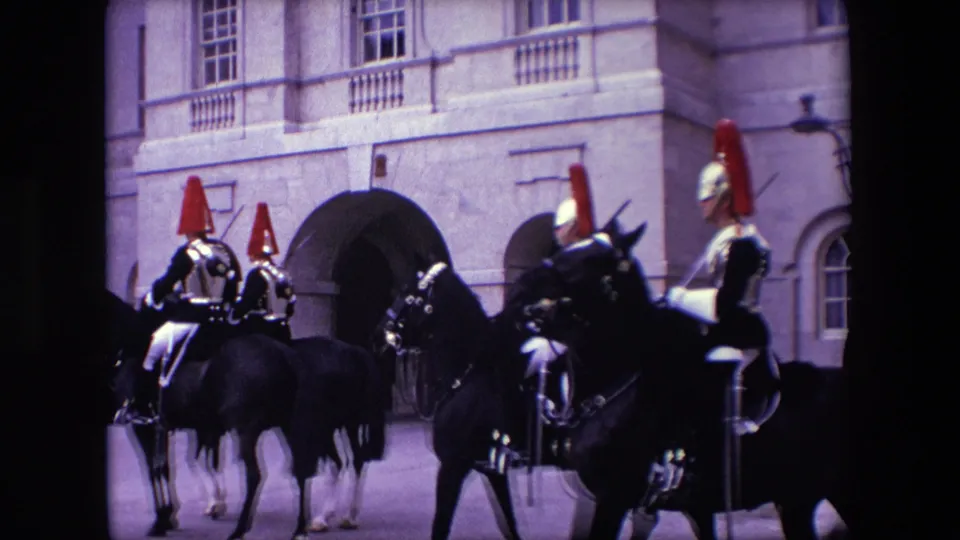 A closer 1967 London frame shows multiple mounted ceremonial riders in armor and red plumed headdresses crossing in front of an arched stone entrance, with the home-movie framing partly obscured by movement.