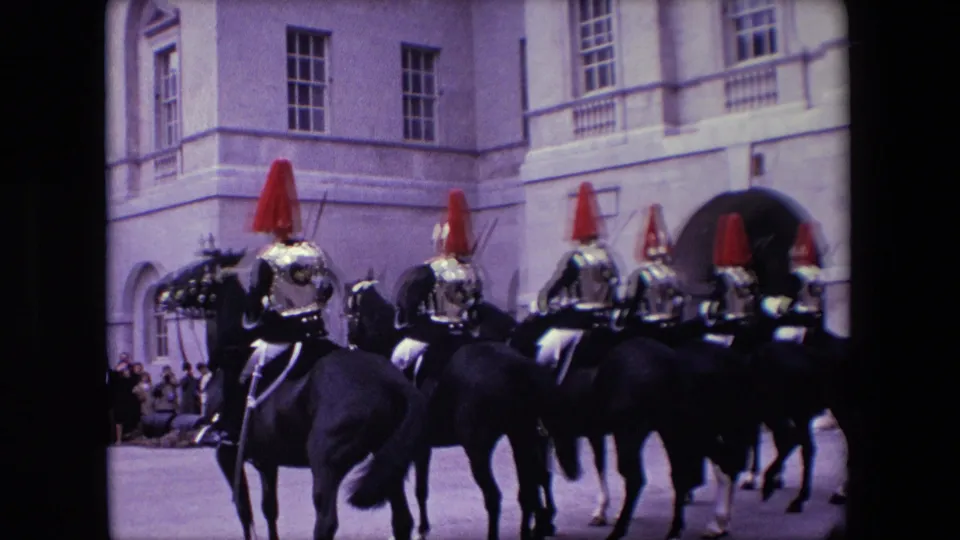 1967 London frame with mounted uniformed riders in polished ceremonial gear moving in formation across a paved area as spectators watch from the side.