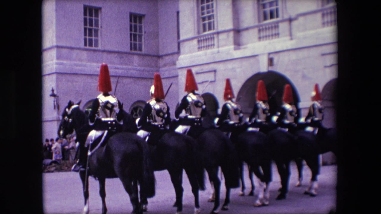 1967 London home-movie frame showing uniformed mounted guards with red plumes riding black horses past spectators outside a formal stone building.