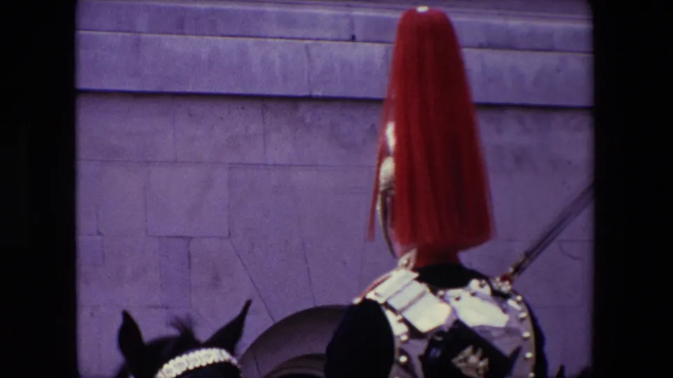 1967 London 8mm frame with a rear view of a ceremonial mounted guard in armor and red plume, with the horse partly visible against a stone building.