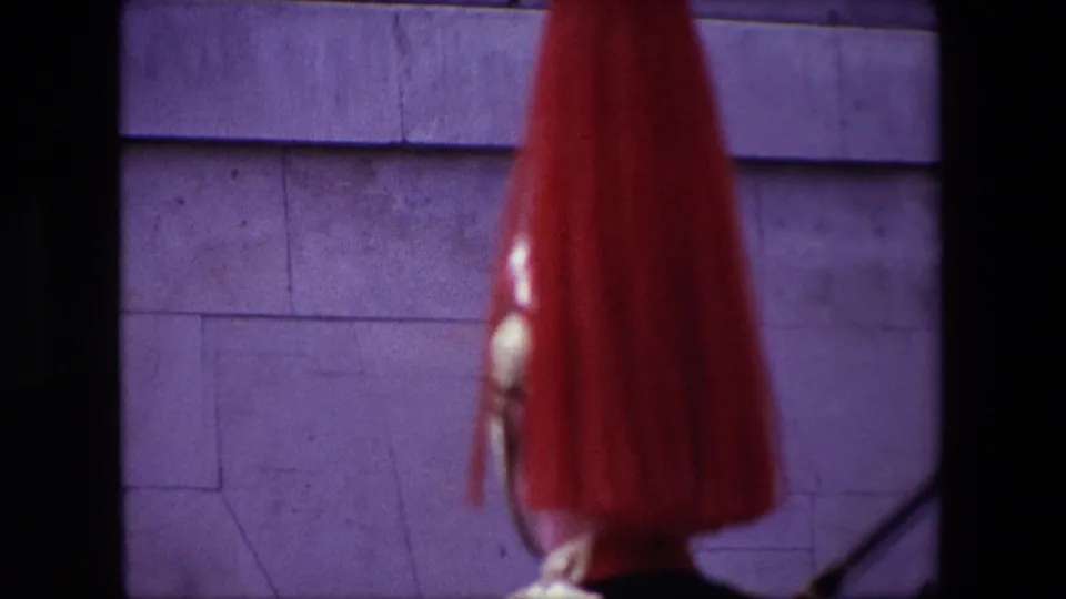 1967 London 8mm frame showing a soft-focus red guard plume and partial armor near a pale stone facade, with the horse no longer clearly visible.