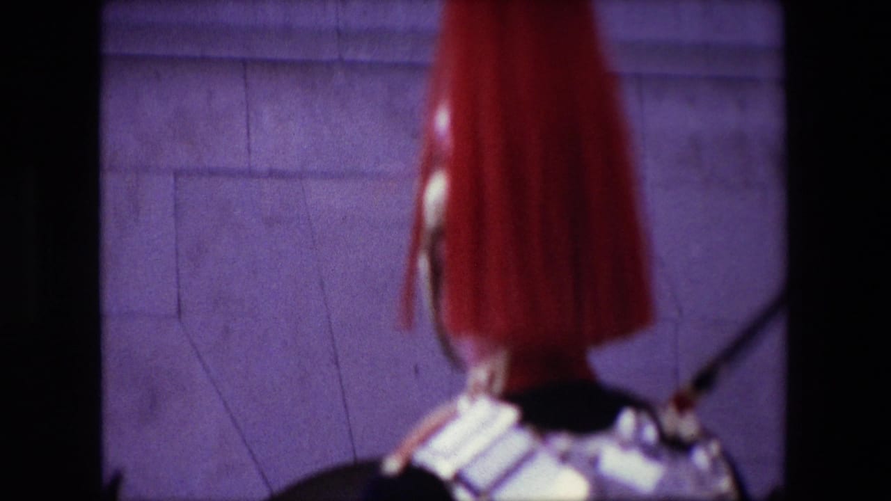Close foreground of a ceremonial guard helmet and shoulder with a building wall behind.