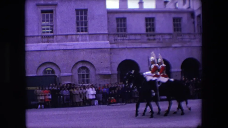 Mounted ceremonial guards in red dress ride dark horses past onlookers outside a large London building in the supplied 1967 home-movie footage.