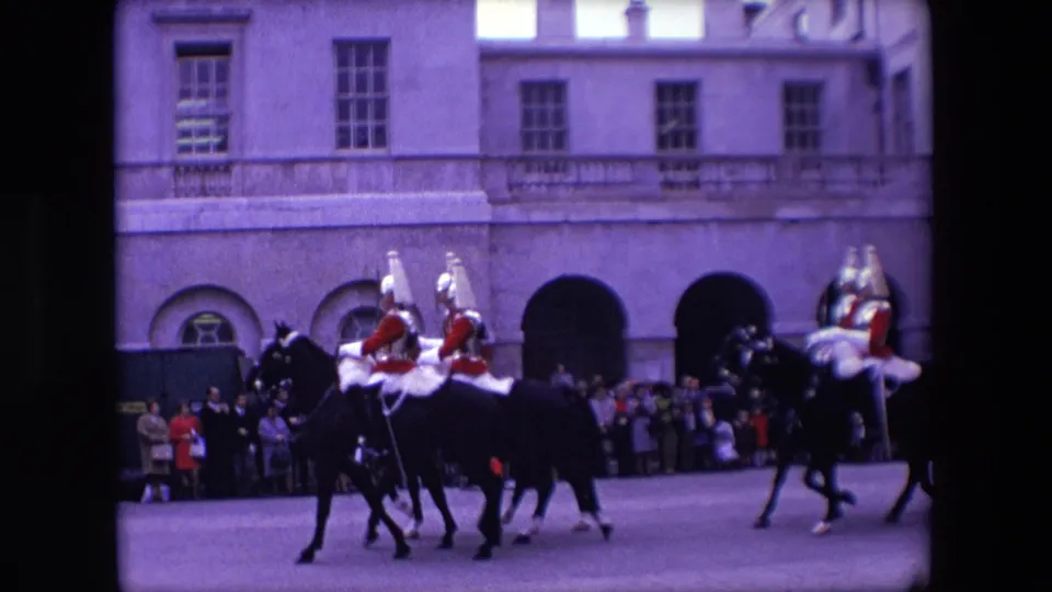 A small formation of mounted ceremonial guards moves across the street while spectators watch from the pavement in 1967 London home-movie footage.