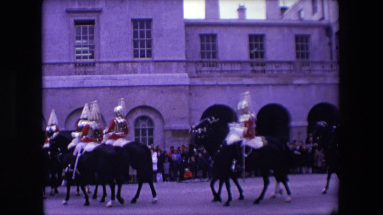 Mounted guards in red and white ceremonial dress continue across a London courtyard while spectators stand near the arched stone facade.