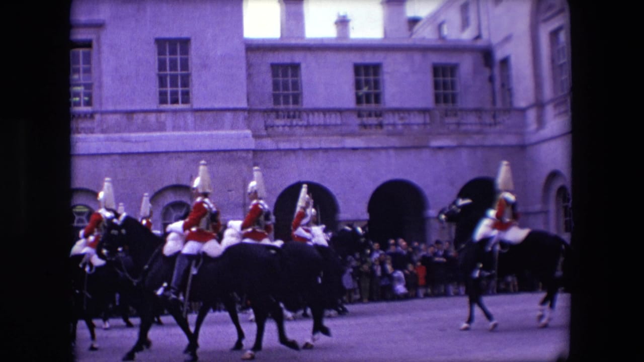 Cavalry riders continue along a paved street with spectators gathered by arched doorways.