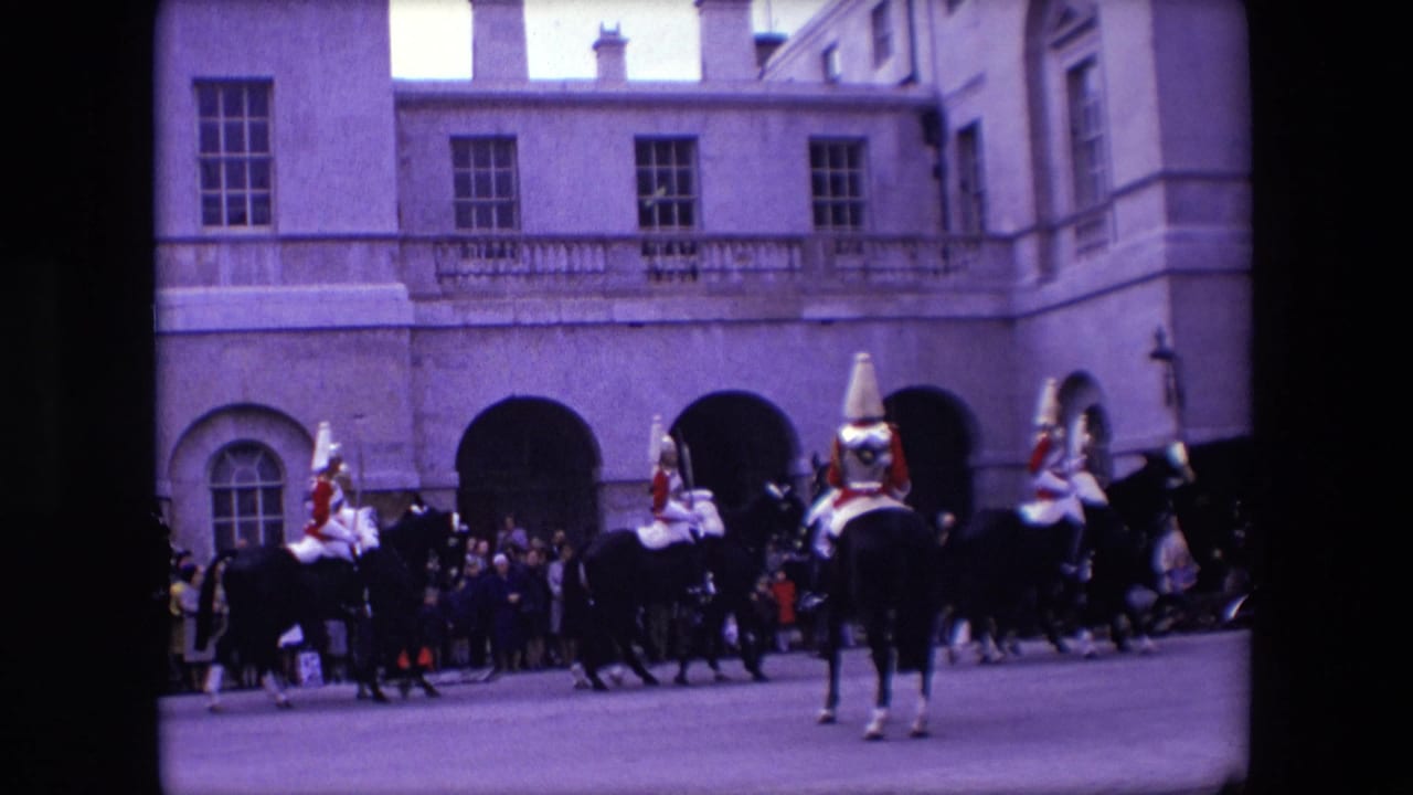 1967 London home-movie frame showing mounted uniformed personnel in red jackets moving past a crowd in front of a formal stone building.
