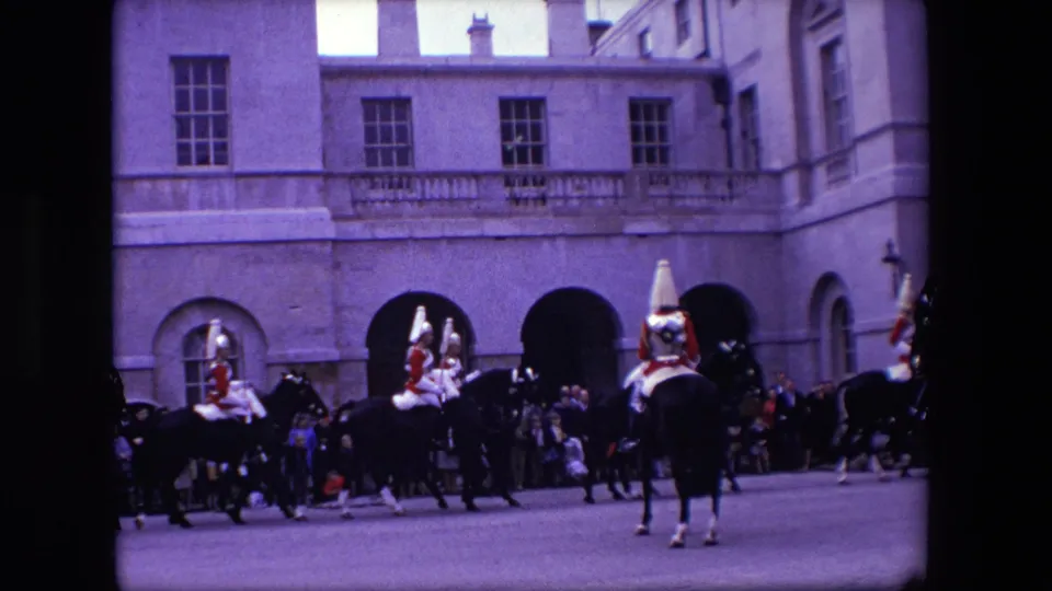 1967 London frame with several mounted ceremonial personnel crossing the foreground while spectators stand near arched openings of a large stone building.