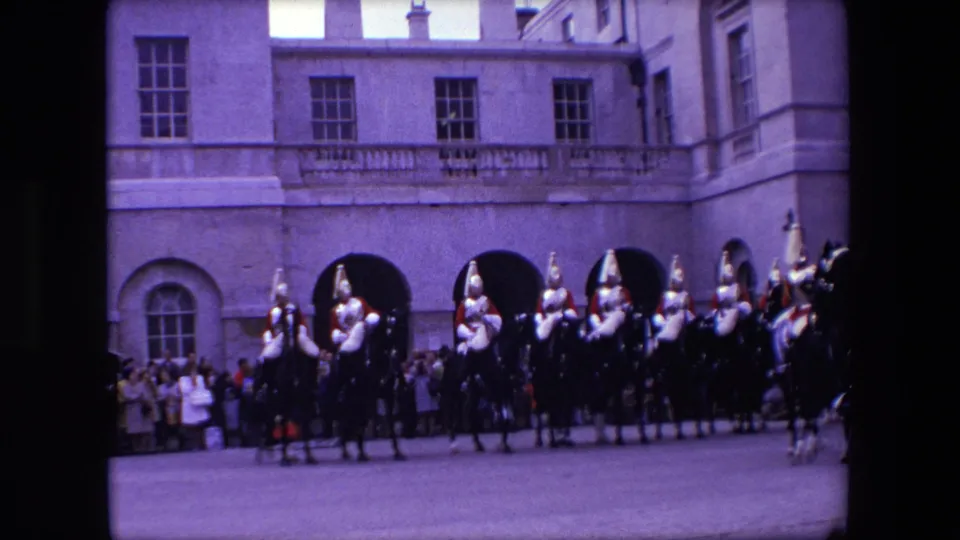 1967 London footage frame with mounted ceremonial guards forming up before the palace arches as visitors watch.