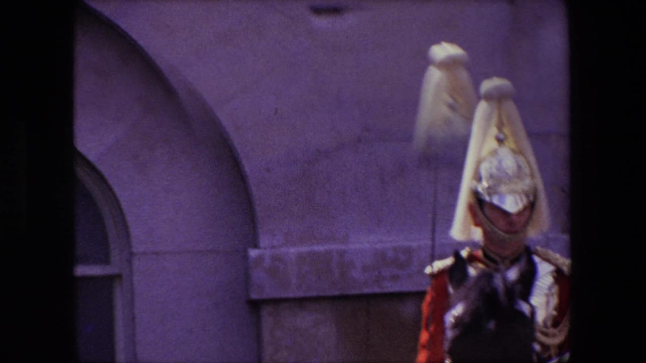A mounted ceremonial guard in London appears in close view wearing a plumed helmet and red uniform against a stone building facade in 1967 home-movie footage.