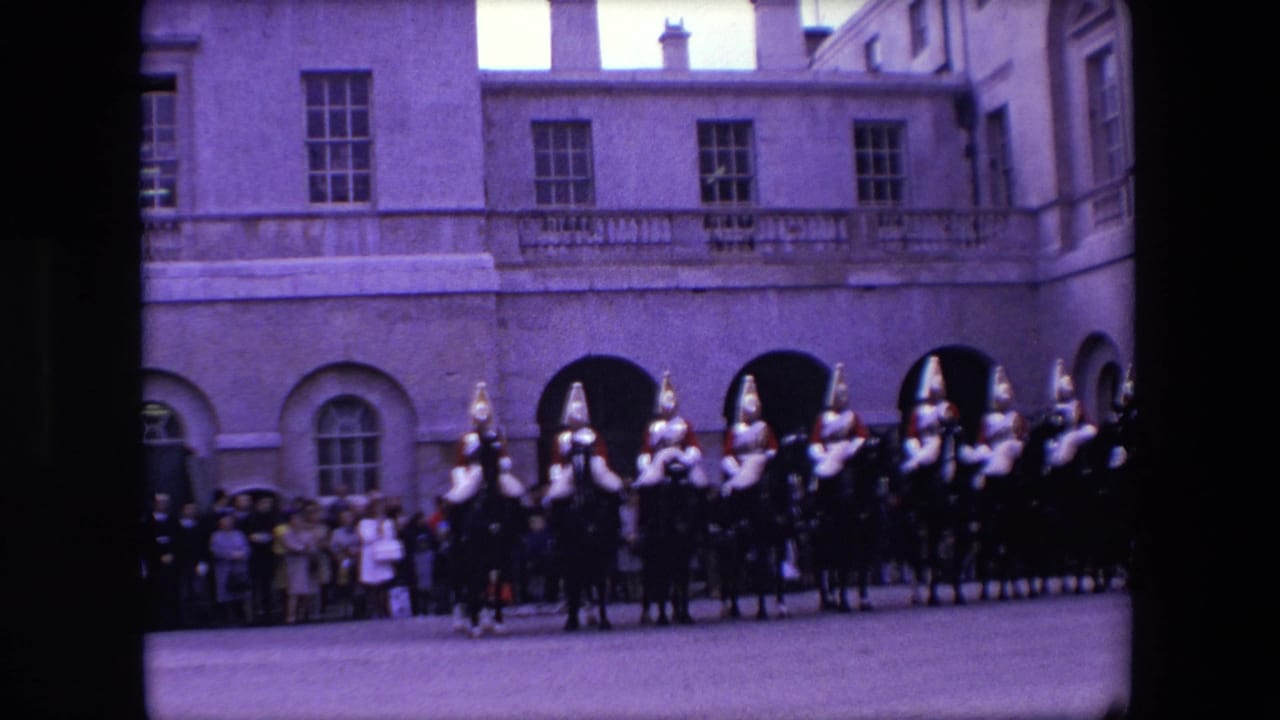 1967 London 8mm frame showing mounted ceremonial riders in plumed helmets moving past spectators outside a formal stone building.