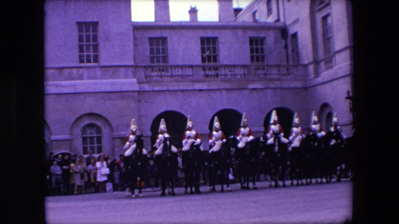 Line of mounted uniformed riders moves across a paved courtyard before a watching crowd.