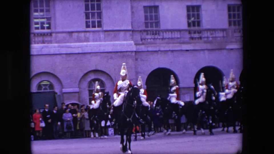 1967 London home-movie frame showing a mounted ceremonial rider facing the camera with other riders and spectators outside a formal building.
