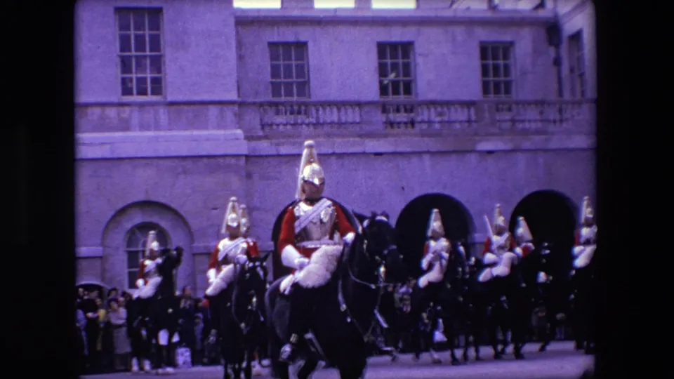 Mounted Queen's Guard soldiers ride in formation before spectators and arched stone architecture in 1967 London home-movie footage.