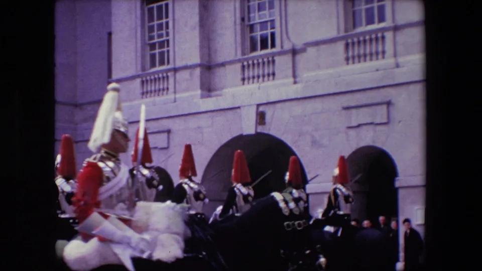 Mounted guards with red and white plumed helmets move through a formal London courtyard against a pale stone facade in 1967 8mm footage.
