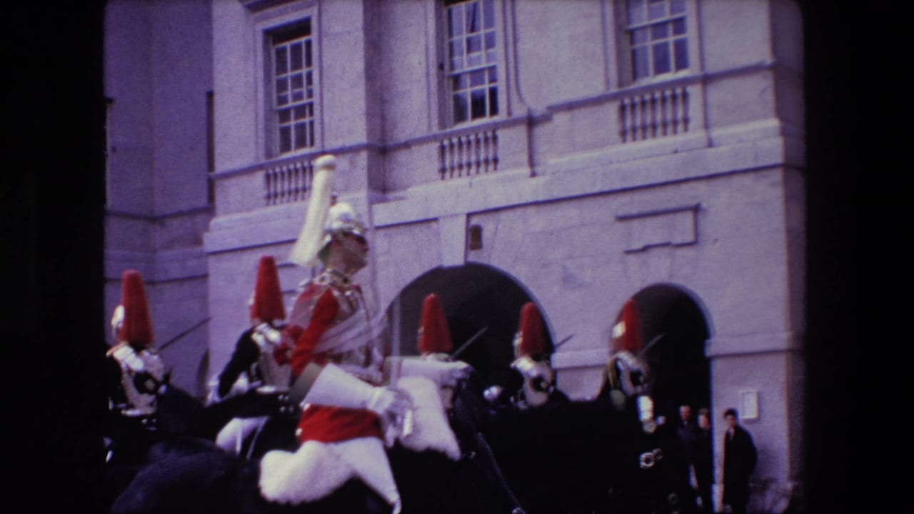 1967 London home-movie frame with a mounted guard in red and white ceremonial dress in the foreground and other helmeted riders behind him near arched stone entrances.