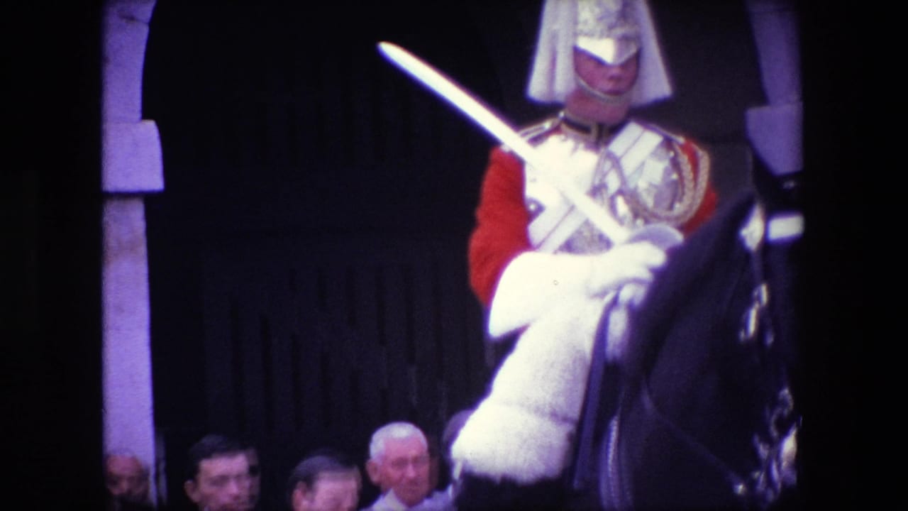 1967 London home-movie frame showing a mounted ceremonial rider in red uniform holding a sword, with spectators partly visible beside a stone arch and dark doorway.