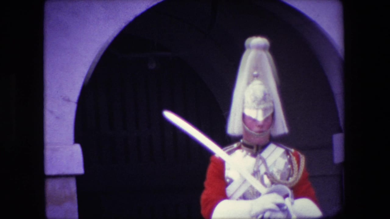 1967 London home-movie frame showing a Royal Guard in ceremonial uniform holding a sword in front of a dark arched entrance.