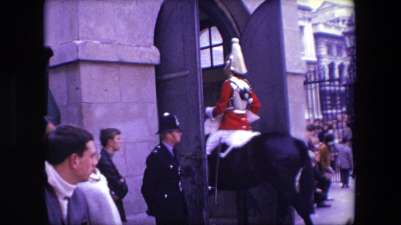 1967 London home-movie frame showing a mounted ceremonial rider in red uniform and armor moving through a stone entrance as spectators watch nearby.