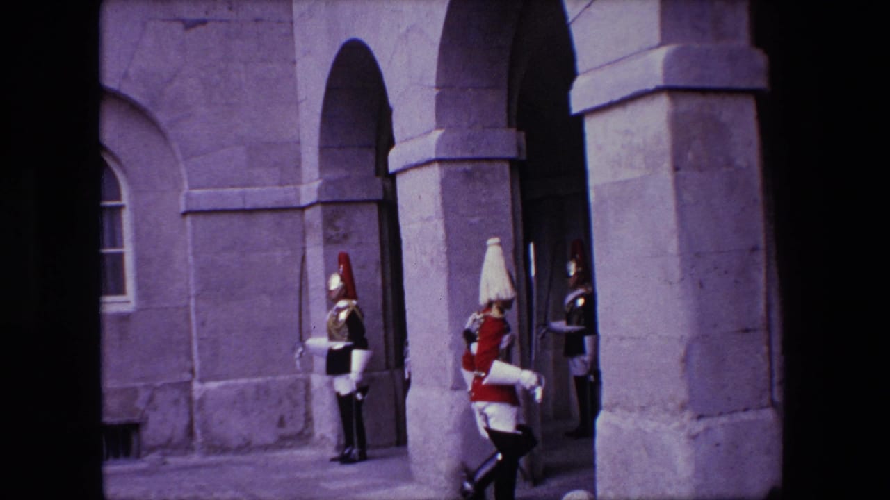 A soldier in a white uniform marches past guards by a stone entrance.