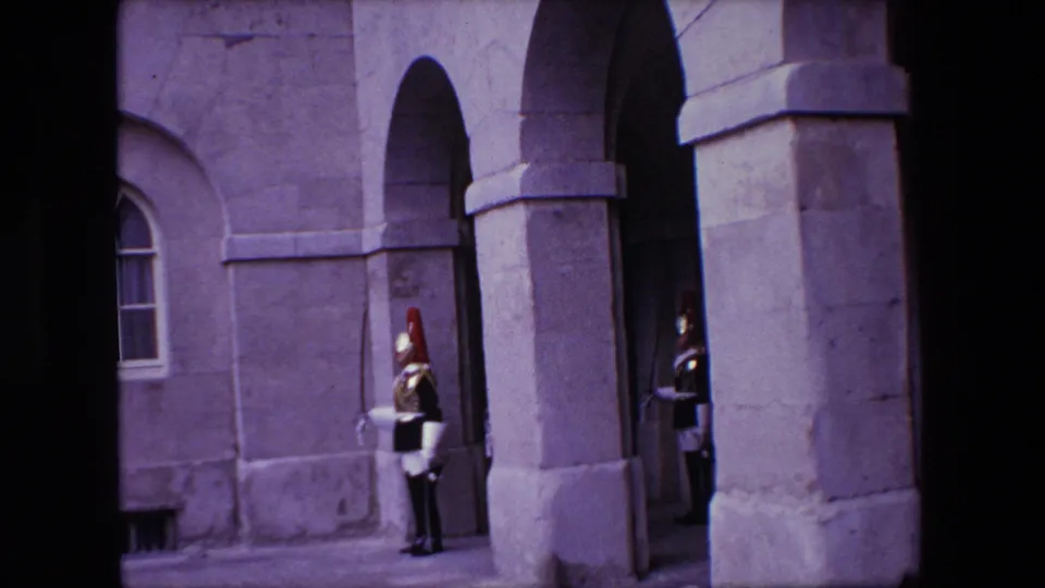 1967 London home-movie frame with a ceremonial guard standing at attention beside a stone arch and doorway.