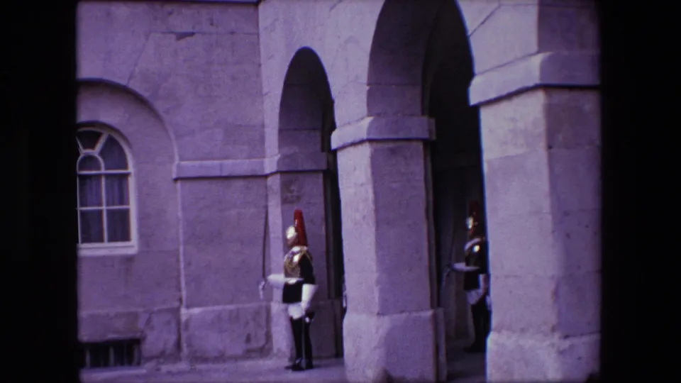 1967 London home-movie frame showing ceremonial guards positioned around a stone arched entrance and masonry facade.