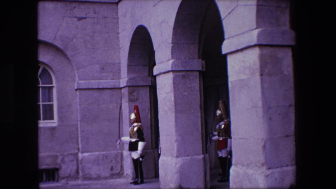 1967 London 8mm frame showing a uniformed guard standing by arched stone architecture outside a formal building.
