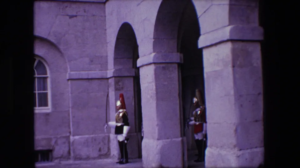 1967 London 8mm frame showing a uniformed guard standing by arched stone architecture outside a formal building.