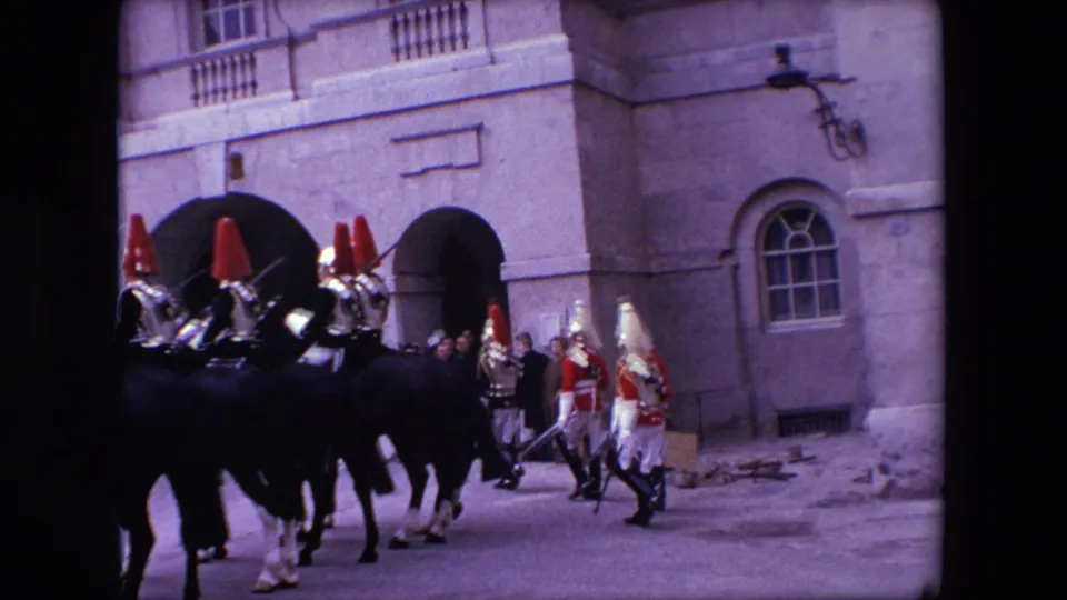 1967 London 8mm frame with mounted ceremonial guards at left and uniformed foot guards crossing in front of arched windows and a stone wall.