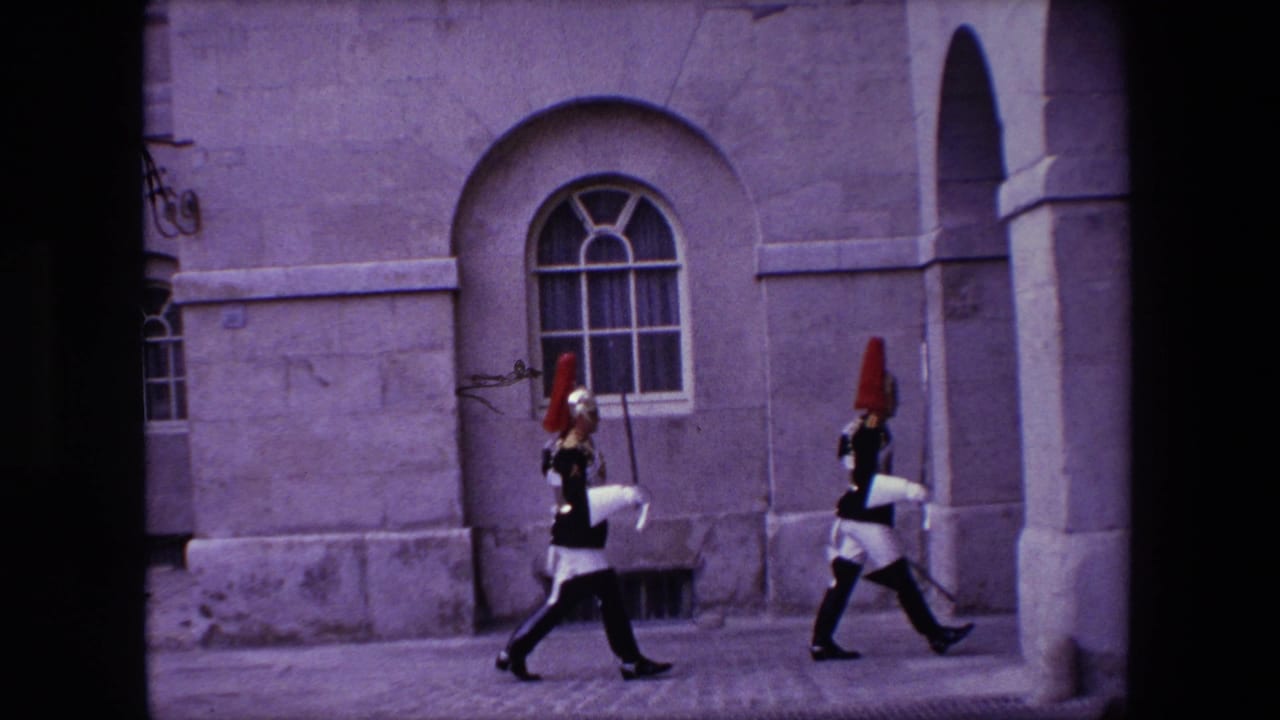 Two ceremonial soldiers in dark uniforms and red-plumed helmets march across a London stone courtyard in 1967 home-movie footage.