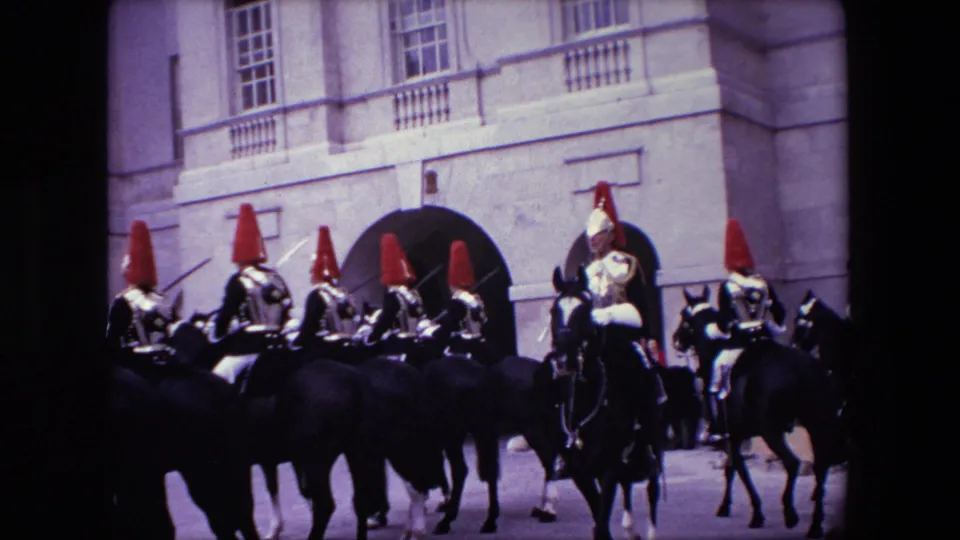 Mounted ceremonial guards in red-plumed helmets ride dark horses near arched stone entrances in 1967 London footage.