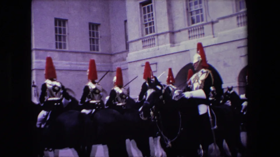 A line of mounted ceremonial guards with red plumes moves across a stone courtyard in London, filmed on 8mm in 1967.