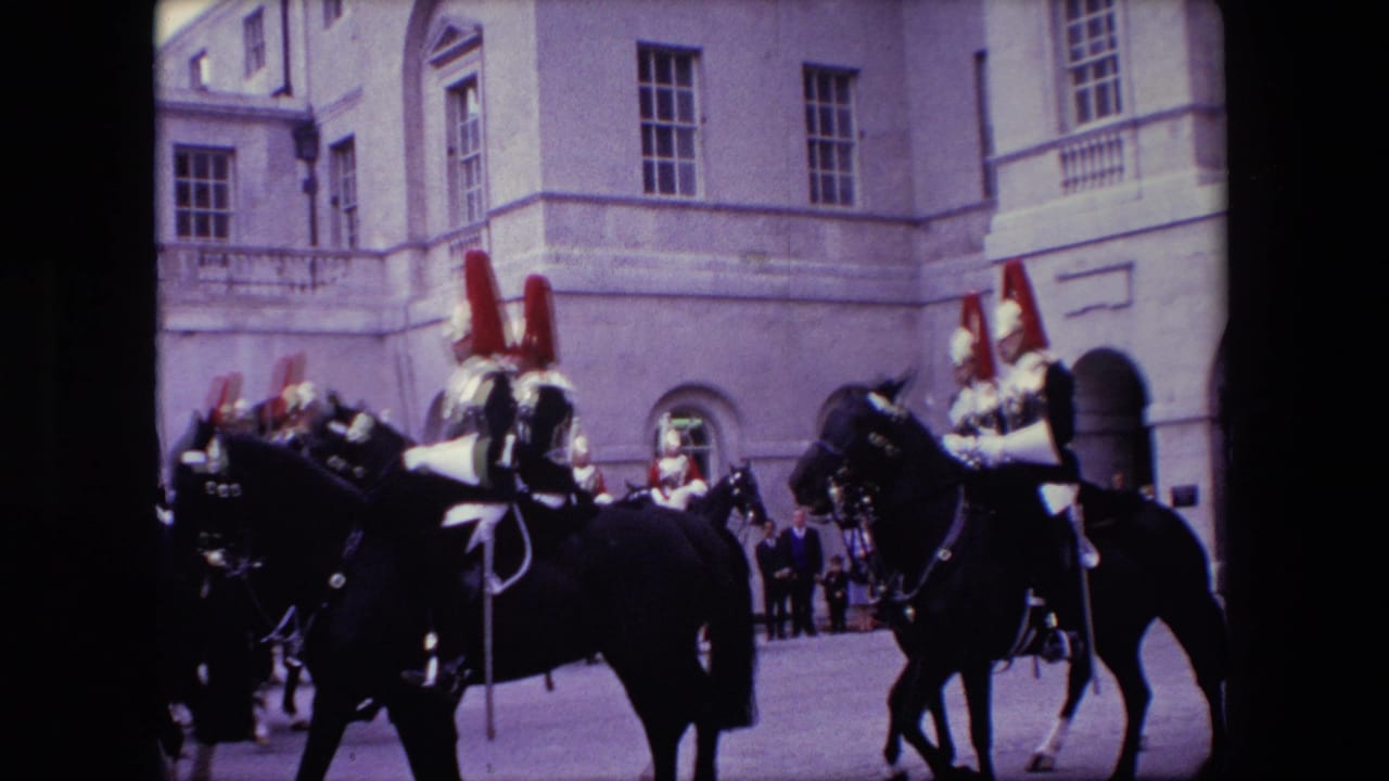 Several mounted guards ride through a courtyard beside a large stone building.