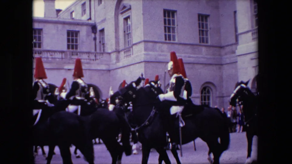 A closer 8mm view shows mounted ceremonial guards with red plumes and dark horses clustered in front of a pale stone London building facade.