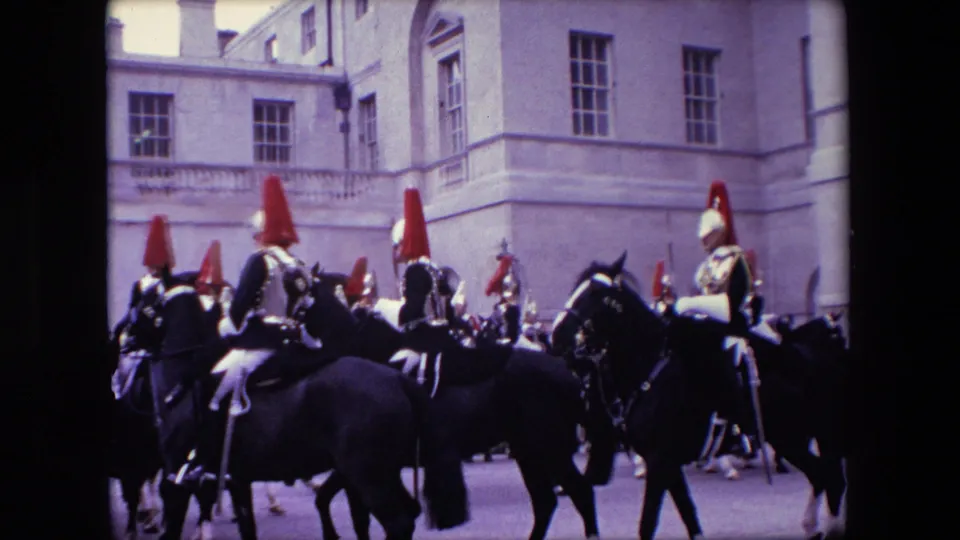 London 1967 archival 8mm footage shows uniformed mounted guards riding across a courtyard, framed by a pale stone facade and watching visitors in the background.