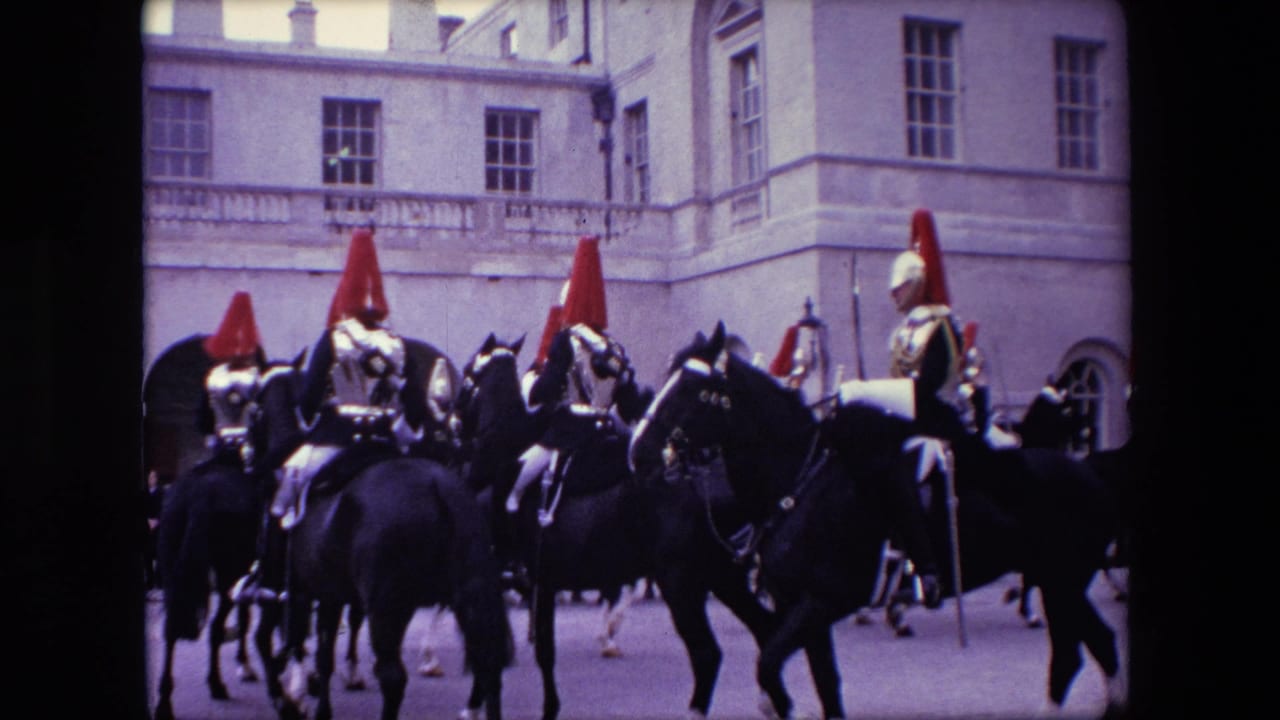 1967 London home-movie frame showing mounted guards with red helmet plumes riding dark horses past formal stone architecture.