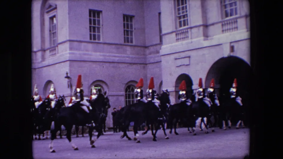 The closing frame shows mounted guards on dark horses moving past a large arched opening in a formal London building facade.