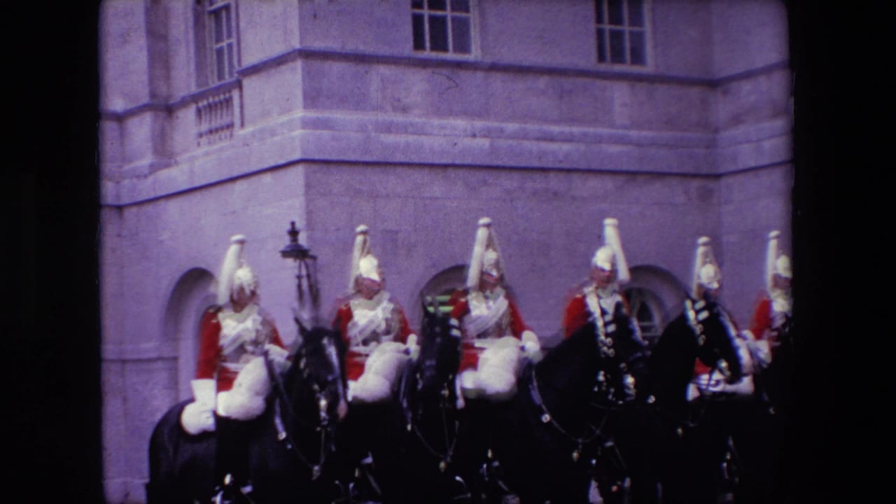 Uniformed mounted guards ride past a stone building facade.