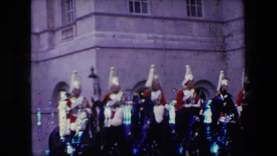 The mounted ceremonial group continues across the courtyard in the London home-movie clip, with horses and uniformed riders partly obscured by soft focus and film artifacts.