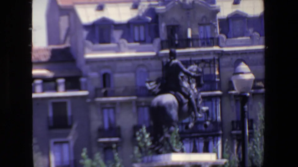 1967 Madrid frame with a mounted statue, a streetlamp, balconies, dormer windows, and pale stone building facades behind it.