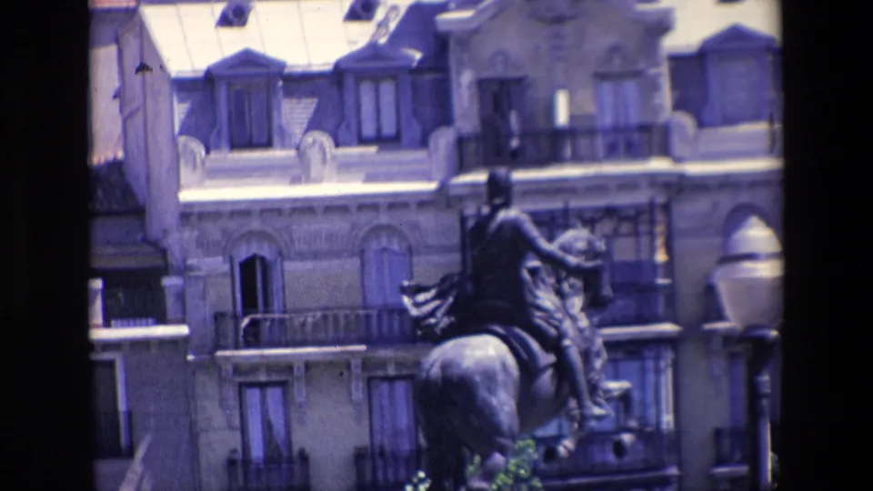 Madrid home-movie frame from 1967 showing the rear of an equestrian statue with balconies, tall windows, and mansard-like roof details in the background.