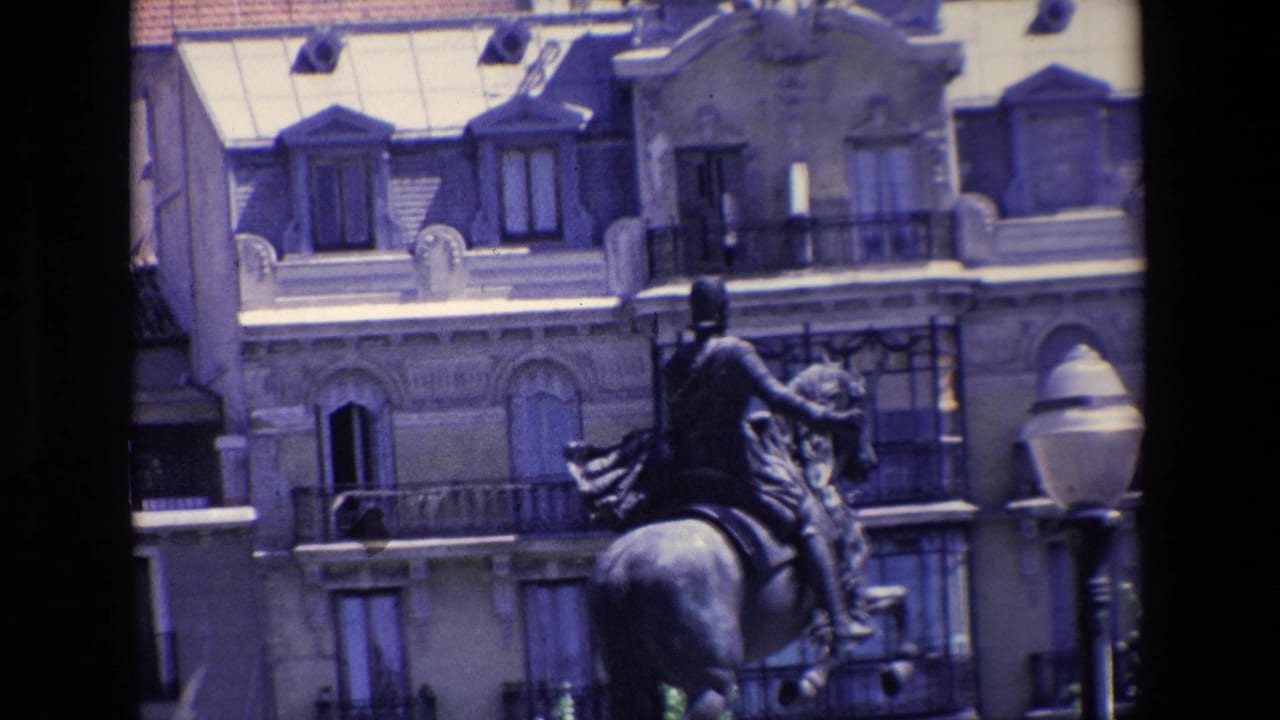 1967 Madrid home-movie frame showing an equestrian statue in front of ornate urban buildings, partly obscured by dark vertical foreground elements.