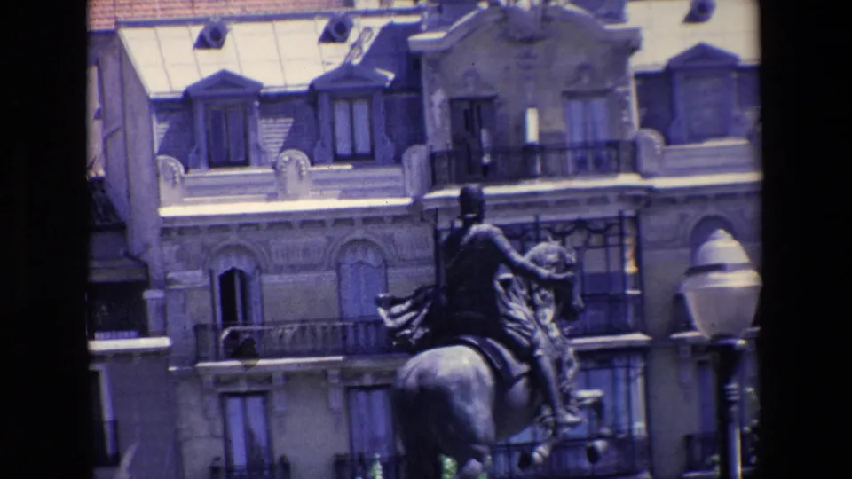 1967 Madrid home-movie frame showing an equestrian statue in front of ornate urban buildings, partly obscured by dark vertical foreground elements.